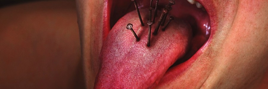A close up of a man sticking out his tongue and there are nails embedded in it