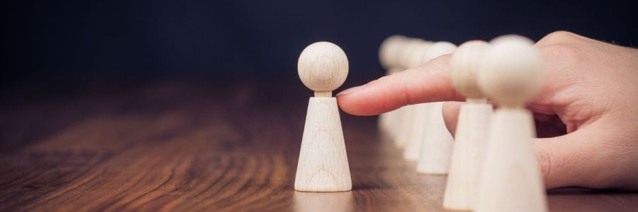 The close up of a wooden pawn being pushed ahead by an index finger out of a row of pawns