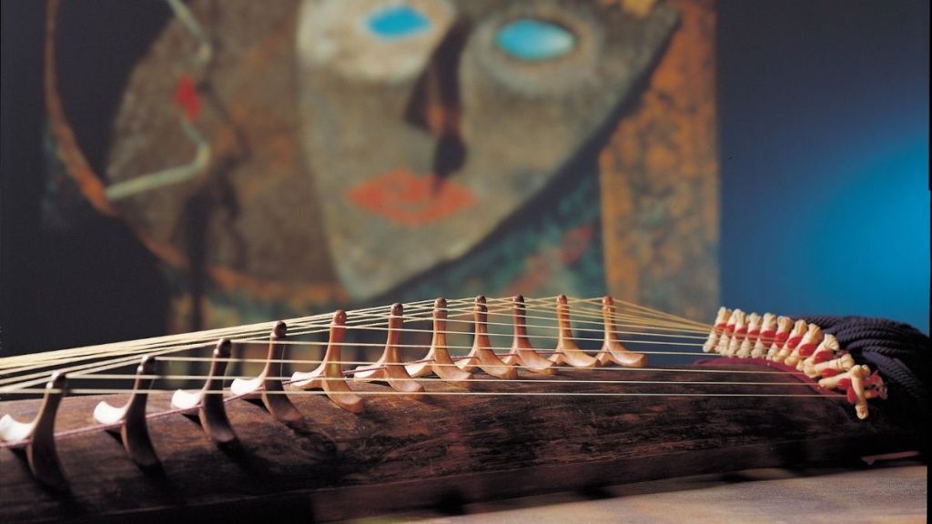 A koto 'Japanese stringed Instrument' lying in the foreground with an abstract face painted in the background