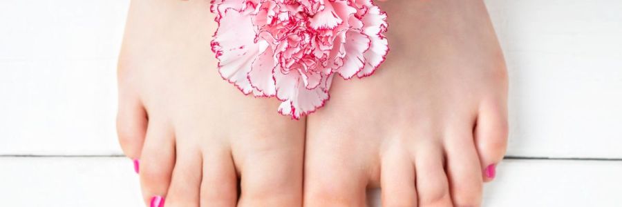 The close up of a woman's pink painted fingernails and toenails with a pink carnation flower positioned between both